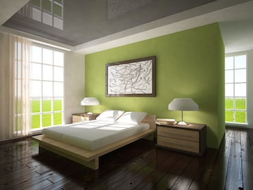 room with a hardwood floor, bright windows on two sides, and a two-person bed with a bedside table and a lamp on each side